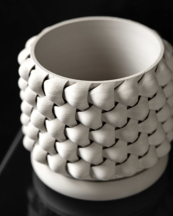 Angled top view of a 3D printed white planter with thick, curved wall structure and intricate repeating braided pattern; open interior emphasizes functional depth and clean print finish inside the rim.