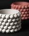 White and terracotta 3D printed planters with matching interwoven texture displayed side by side; the focus is on the foreground white planter showing deep, sculpted layers and a smooth upper rim.