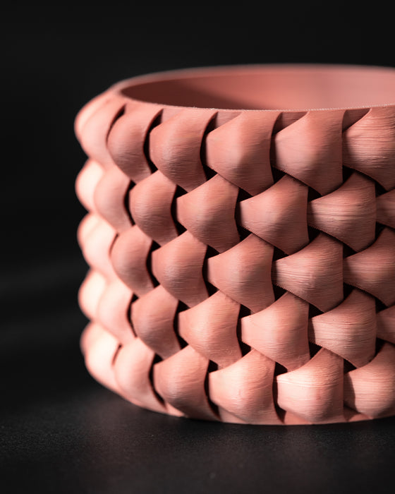 Terracotta 3D printed planter with cylindrical body and bold braided design; close-up highlights warm earthy tone and tightly layered diamond segments with soft sheen from filament lines.