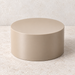 Beige round plant stand with a flat closed top and straight cylindrical sides, shown on a light stone surface.
