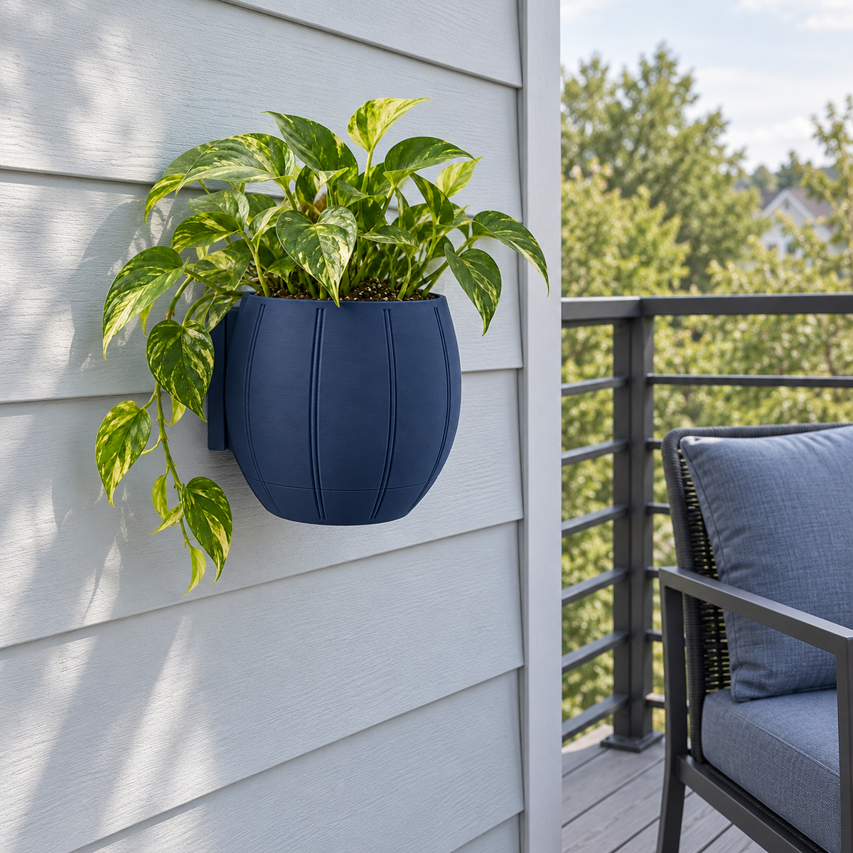 Navy Duoro wall planter with golden pothos on a gray-blue balcony wall beside a graphite outdoor chair.