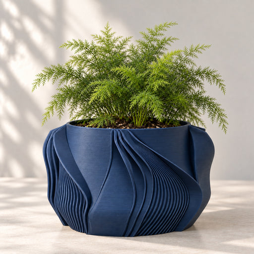Navy blue Fano geometric planter with green foliage and sweeping fan-shaped folds on a pale surface.