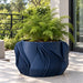 Navy blue Fano planter with green foliage on a sunlit patio beside a railing.