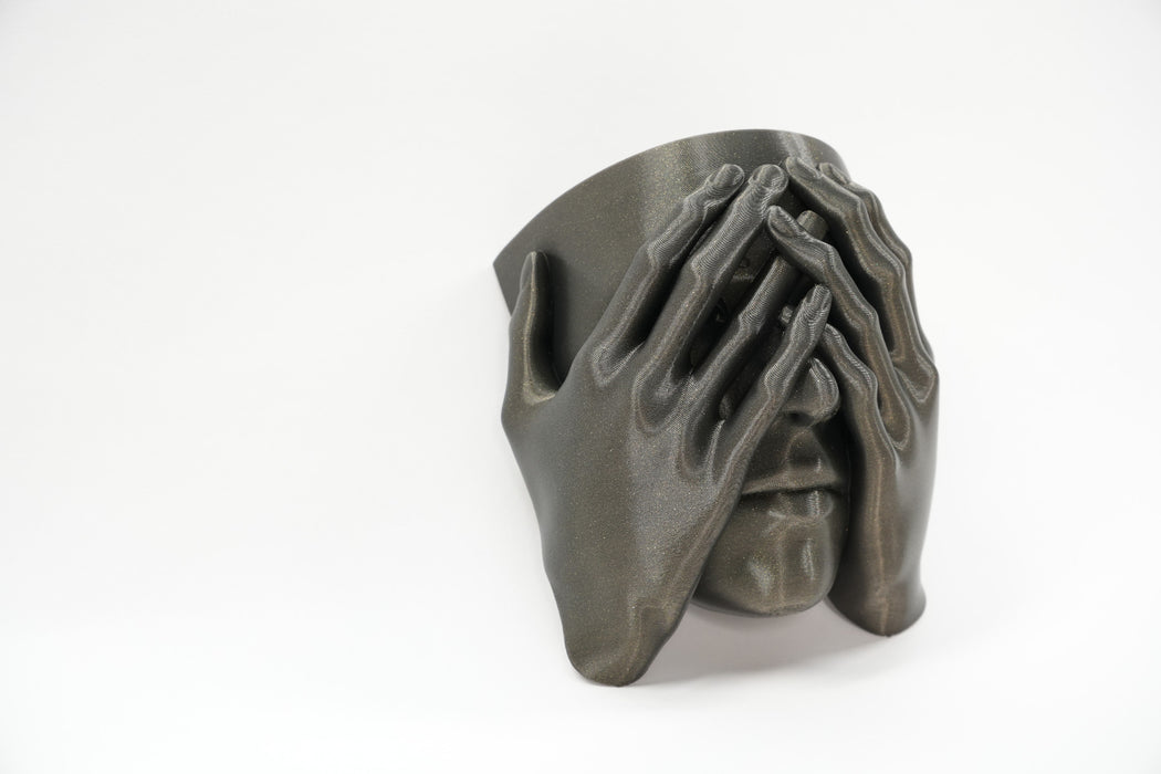 Side angle of a sculptural face wall planter with dimensional hands and face details
