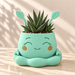 Mint Pika character planter with leaf-shaped ears, smiling face, orange cheeks and a striped succulent.