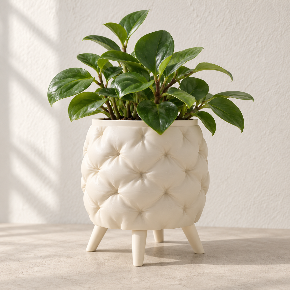 Cream Kivu planter with a padded-looking quilted surface, short legs and green foliage.