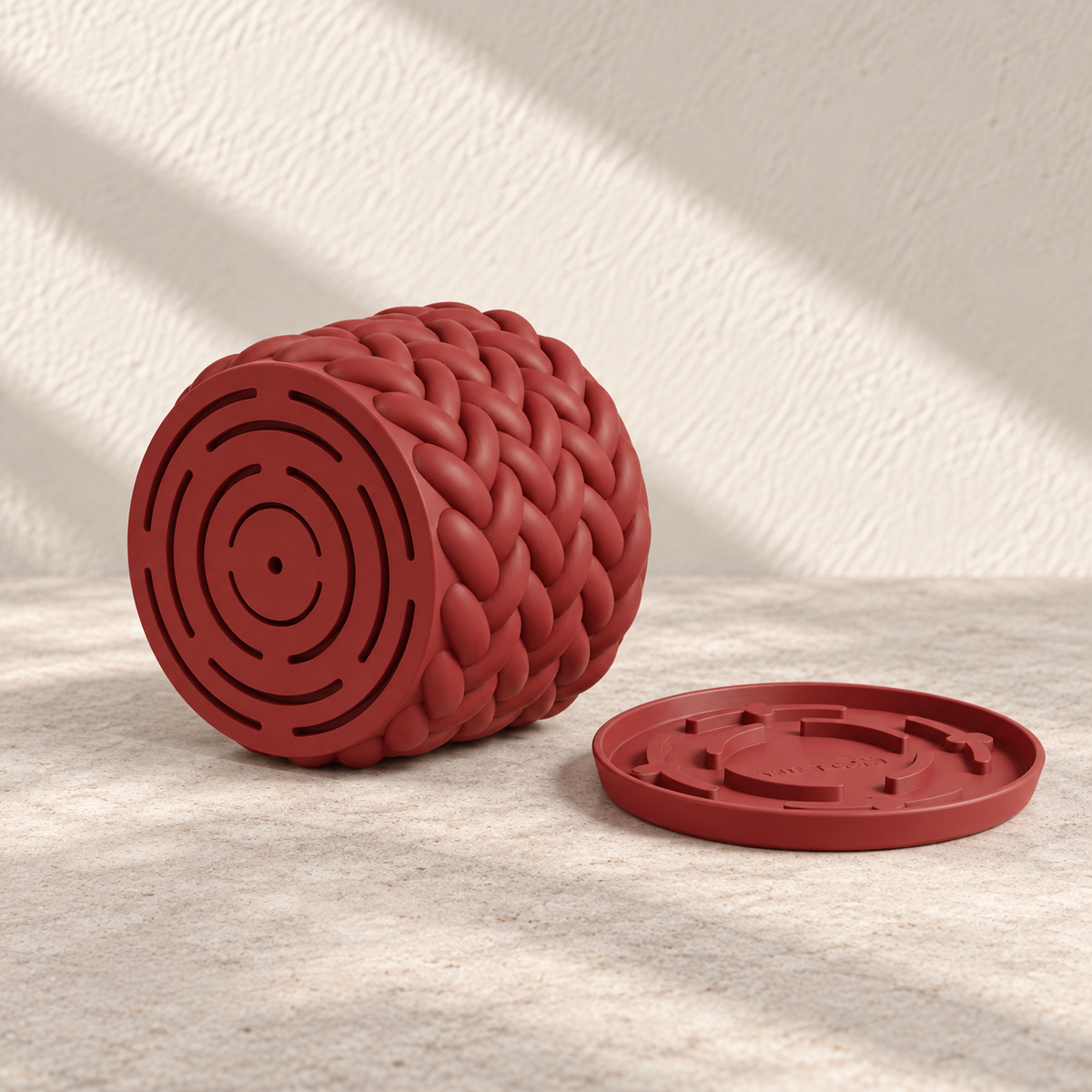 Red Braido planter tipped sideways to show concentric drainage slots, with the detached tray beside it.