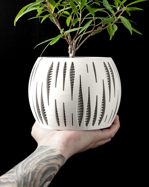 3D printed planter pot with vertical slits and inner lattice, spherical form held in tattooed hand, decorative plant inserted, white modern geometric flower pot with perforated pattern, minimalist home decor, unique planter design, gifts for plant lovers, round indoor pot, futuristic aesthetic container for succulents or bonsai