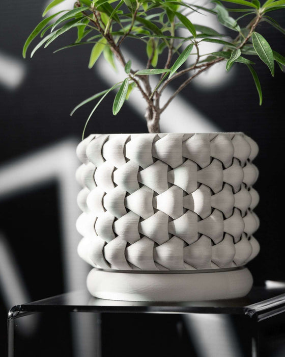 Modern white 3D printed planter with lush green plant, placed on sleek pedestal; clean lines, consistent weave texture, and a smooth base make this planter a standout piece for contemporary decor.