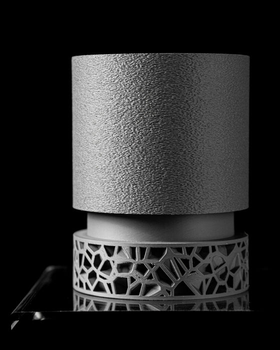 angled view of a large textured 3D-printed pot on a cutout support ring, showcasing craftsmanship of modern additive manufacturing, the body is clean and upright with stone-like feel, while the base is geometric, asymmetric, and open, providing a play of shadows and form, great for upright or ornamental plants, design object for interiors, planter pot, 3d printed planter, housewarming gift, college gift, personalised planter, black and grey modern decor, unique flower pot, plant pot
