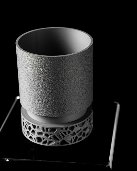 close-up of lower section of a 3D printed planter with detailed cutout base structure, showing complex polygonal openings and smooth connector ring, top body features fine-grain vertical texture, color balanced between soft charcoal and graphite, printed with sustainable material, indoor-friendly, decorative and lightweight, modern home planter, sculptural plant pot, black planter, gifts for modern homeowners, 3d printed item, planters and pots, personalised decor, flower pots