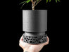 side profile of matte black planter with minimalist cylindrical shape and finely layered texture, designed for elegance and function, standing on an open-patterned architectural base inspired by natural bone structures, 3d printed with eco-friendly PLA, blending art and utility, planter pot, 3d printed planter, decorative flower pot, sculptural container, minimalist planter design, modern texture, interior decor object, housewarming gift, personalised home piece, new home accessory
