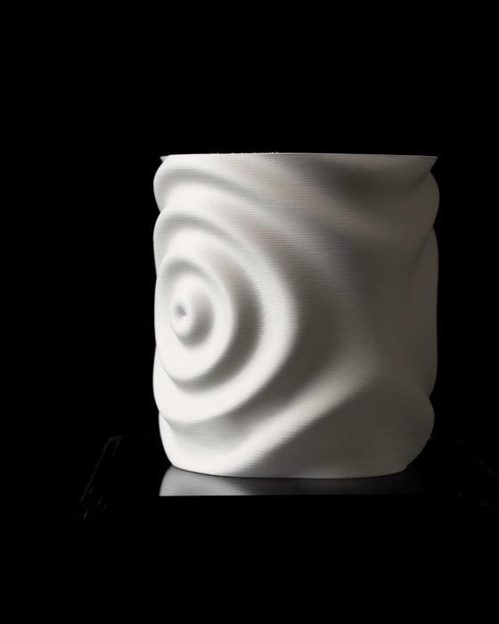 side horizontal shot of hollow 3d printed planter lying on black glass platform, open top revealing smooth inner surface, outer wall features a prominent circular ripple relief, resembling drop-induced water waves, dynamic yet balanced sculptural form, ideal for contemporary plant styling, sustainable 3d printed home decor accent, matte white texture reflects light softly