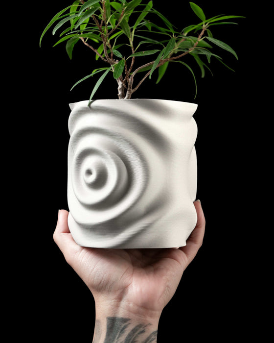hand holding white 3d printed planter with water ripple design on outer surface, green plant growing from top, organic asymmetrical shape with digitally precise curves, lightweight material and smooth matte texture, functional art object for modern homes, expressive yet calming design, suitable for gifts or eco-conscious decor setups
