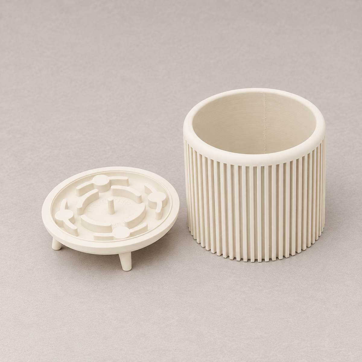 Cream Quadra planter beside its detached circular base with short legs.