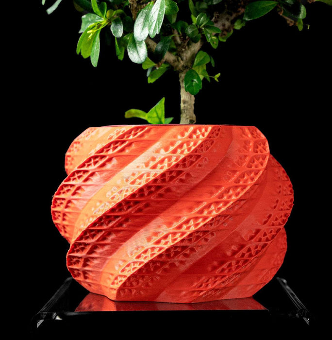 A vivid coral red planter pot with sculptural details, resting on a matching base. This 3D printed planter is perfect for succulents, bonsai, or indoor greenery, adding a modern twist to traditional flower pots. Great for unique home decor, gifts for mom, or book plant pot display, it's a standout among indoor planters and low planter pots with unique flair.