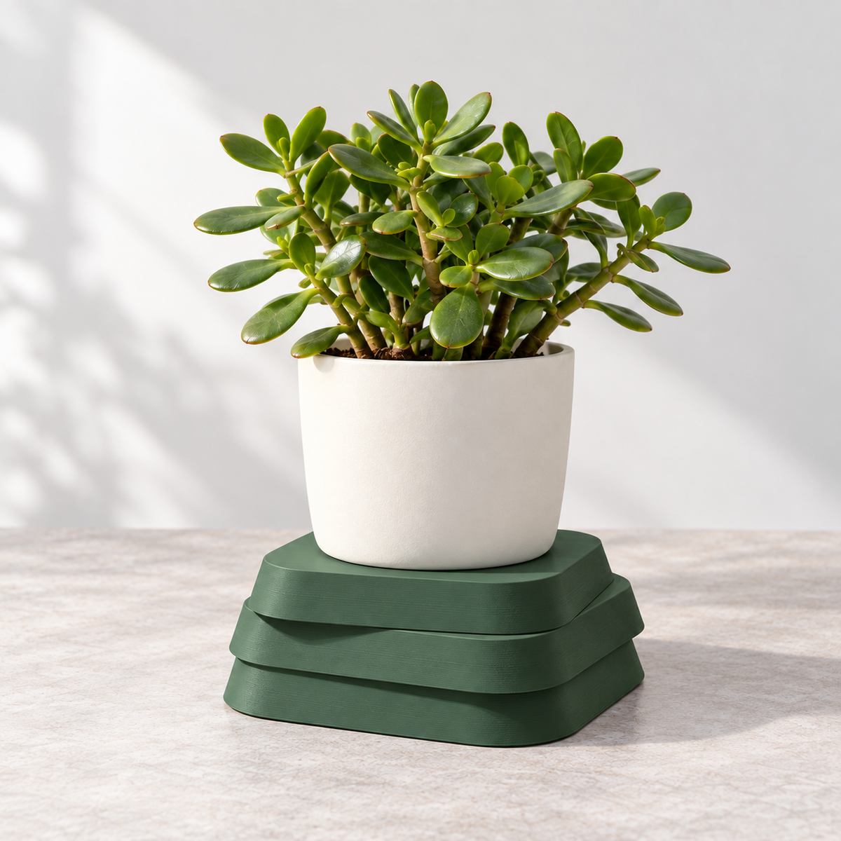 Green three-layer plant pedestal holding a white planter with a jade plant on a light tabletop.