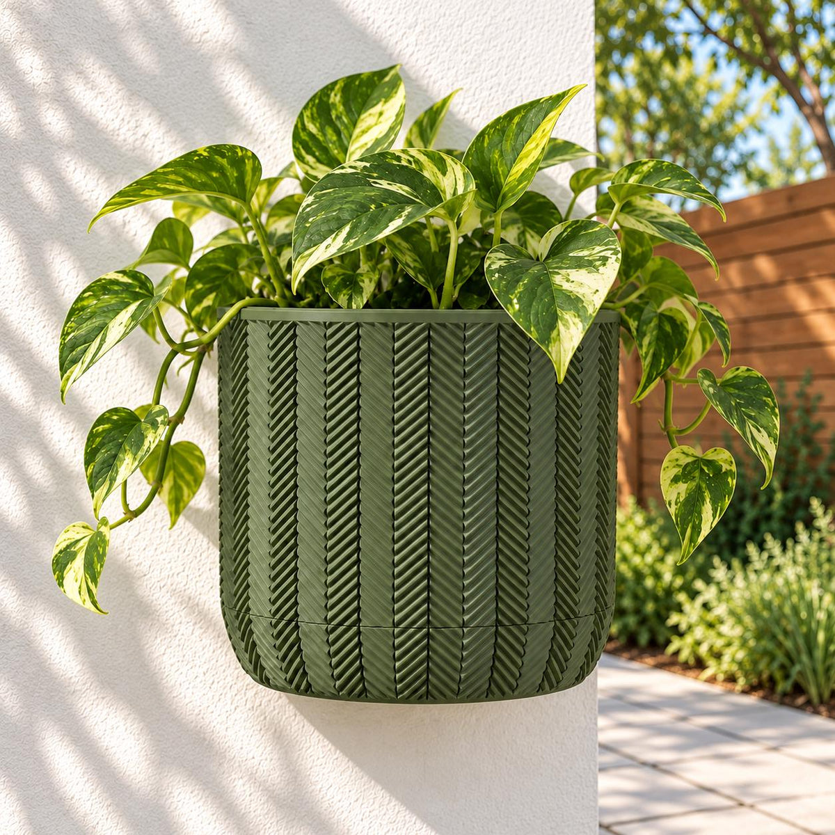 Army green Spigo wall planter with trailing pothos on a white patio column beside a wooden privacy screen.