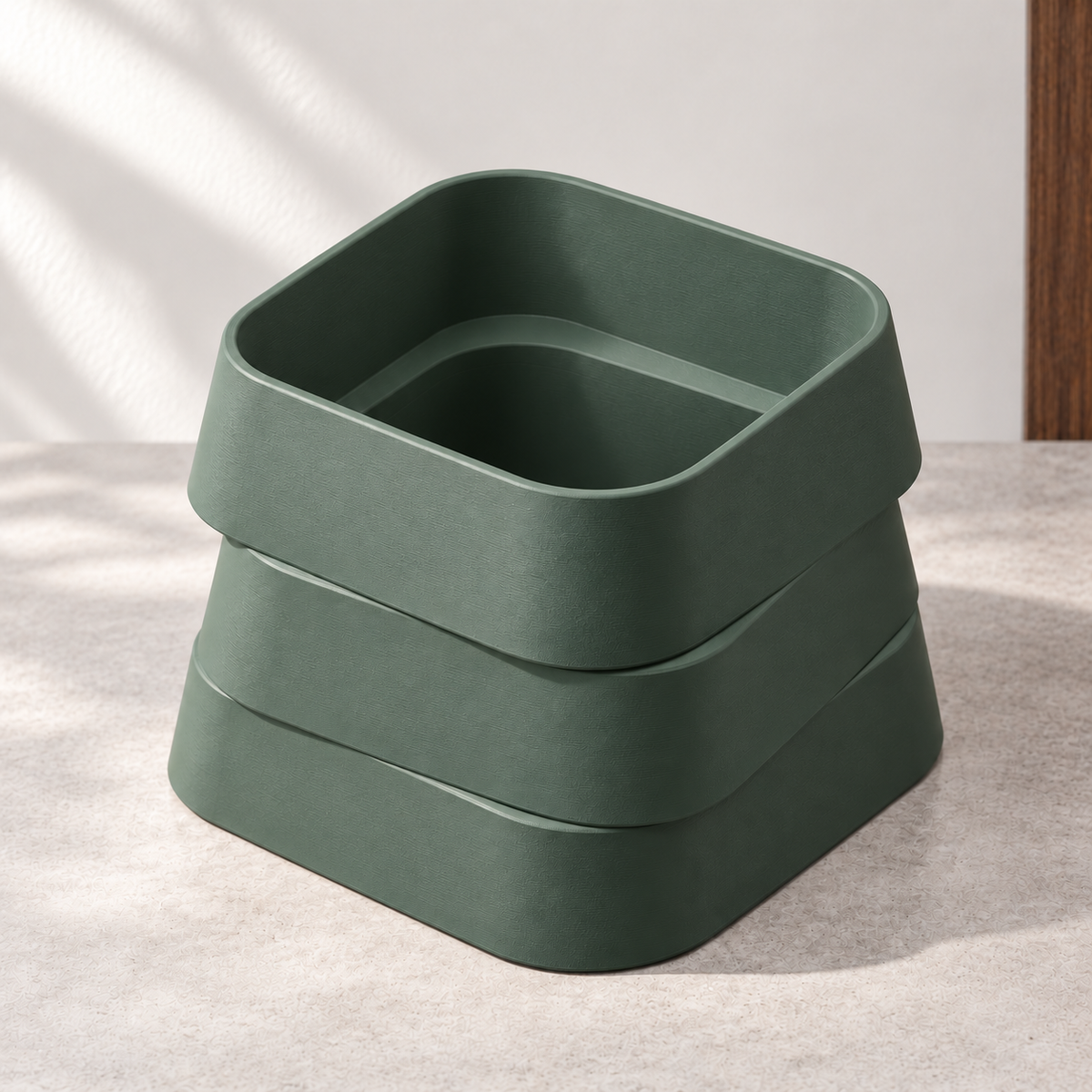 Design visualization of an empty Forest Green planter with three offset rounded-square tiers, viewed from above on a pale gray surface against an off-white wall.
