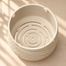 High-angle view inside the cream Tessaro hanging planter, showing smooth inner walls, rim suspension openings and concentric curved drainage slots.