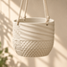Empty cream Tessaro planter suspended by ropes, showing diagonal ridges, raised dots, woven relief and the seam of its removable lower saucer.