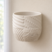 Empty cream Tessaro wall-mounted plant pot showing its textured patchwork surface and the seam of the matching lower drainage tray.
