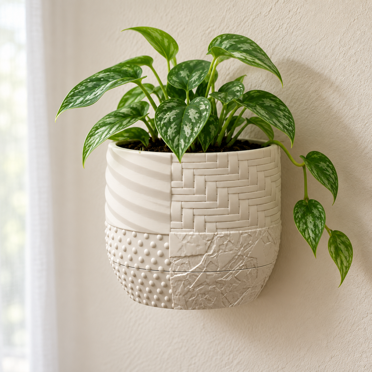 Cream Tessaro wall planter with a green trailing plant, woven panels, flowing ridges, raised dots and crackle texture on a light wall.