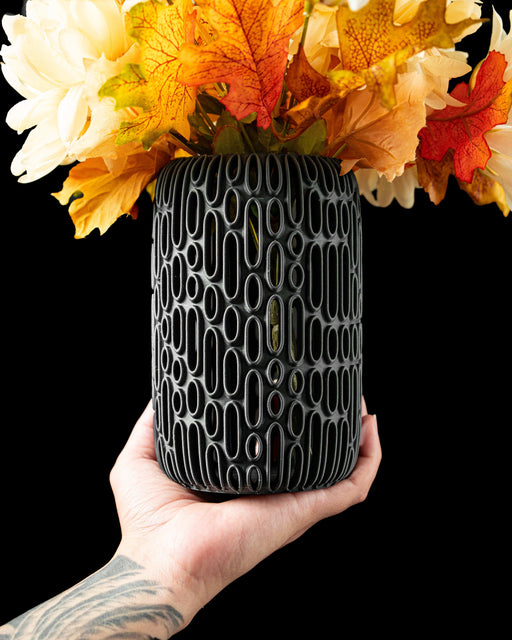 3d printed black vase with intricate vertical oval cutouts arranged in an organic pattern, modern flower vase with futuristic relief design, cylindrical silhouette and rounded base, perfect for dried flowers or decorative stems, unique home decor piece for table or shelf, matte black color highlighting sculptural contours, contemporary vase with detailed textures and structural harmony, vase dried flowers, home office decor, ikebana vase, black vase, vases for flowers, modern vase