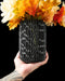 3d printed black vase with intricate vertical oval cutouts arranged in an organic pattern, modern flower vase with futuristic relief design, cylindrical silhouette and rounded base, perfect for dried flowers or decorative stems, unique home decor piece for table or shelf, matte black color highlighting sculptural contours, contemporary vase with detailed textures and structural harmony, vase dried flowers, home office decor, ikebana vase, black vase, vases for flowers, modern vase
