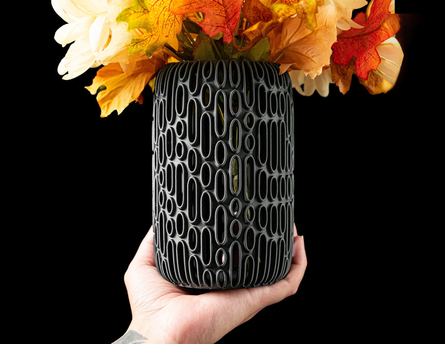 black cylinder-shaped flower vase made with 3d printing technique, showing deep oval indentations forming a dense pattern, ideal vase for dried flowers or tall decorative arrangements, artistic vase design with sculptural texture, modern black vase with perforated surface for unique gift or stylish accent, flower vase with vertical openwork structure, minimalist futuristic vase, ikebana vase, aesthetic vase, black vase, unique home decor, home office vase