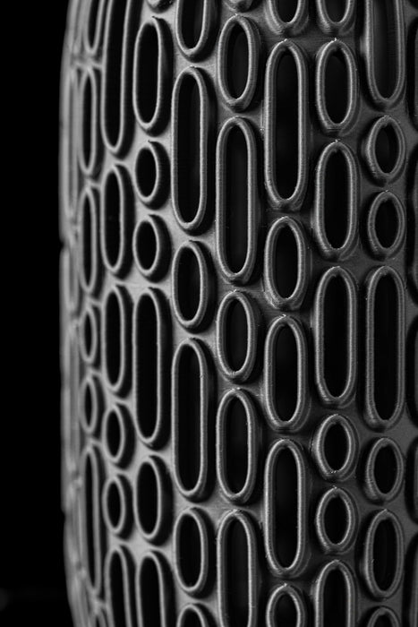 close-up of 3d printed black vase with raised oval grid pattern and matte finish, showcasing intricate craftsmanship and futuristic surface detail, artistic vase with sculptural cutouts and solid core, designed for dried flowers or ornamental stems, modern black cylinder vase with dimensional texture and minimalist style, flower vase, black vase, 3d printed vase, modern flower vase, vase dried flowers, unique home decor