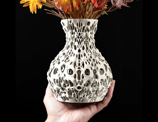 Modern white vase with an organically perforated surface, designed with a dense pattern of rounded and elongated holes that vary in size and placement, creating a lace-like structure; the 3D-printed texture is subtly visible, adding depth to the layered sculptural form; this vase offers a unique combination of fluid silhouette and futuristic design; suitable for dried flowers, decorative stems, or curated floral arrangements.