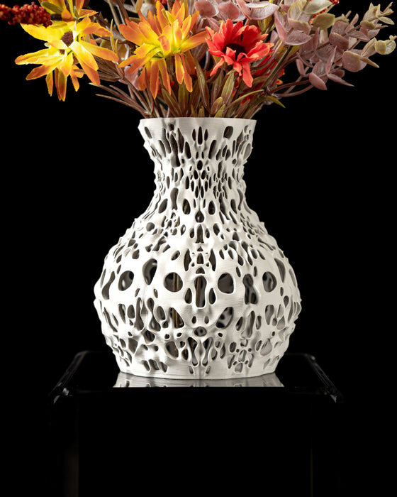 3d printed vase featuring a perforated geometric pattern reminiscent of cellular or porous textures, with a rounded base and a slightly narrowed neck; the surface is evenly pierced with oval and irregular openings that bring visual lightness and intricate detailing; ideal for dried flowers, decorative stems, or curated floral arrangements; the form suggests both chaos and structure, echoing coral reefs.