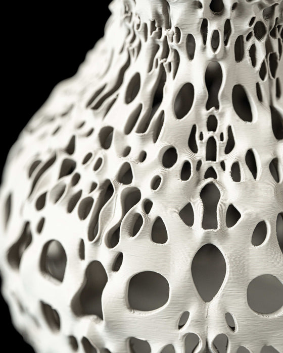 Futuristic home decor vase showcasing fluid curves and clustered negative space, expertly printed using sustainable 3D technology; the honeycomb-like perforations twist along the form, producing contrast between solid material and voids; suitable for dried flowers, decorative stems, or curated floral arrangements; this unique home accent doubles as a sculptural centerpiece.
