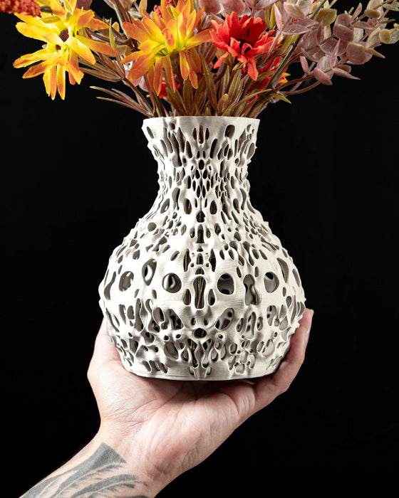 Spherical vase with dramatically sculpted openwork that reveals interior depth through dozens of curved and elliptical perforations; faint horizontal 3D-print striations add character to the smooth matte finish; ideal for dried flowers, decorative stems, or curated floral arrangements; the piece balances complexity and simplicity with a touch of mathematical symmetry.