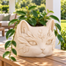Cream white cat planter with trailing hoya on a teak console on a covered outdoor patio