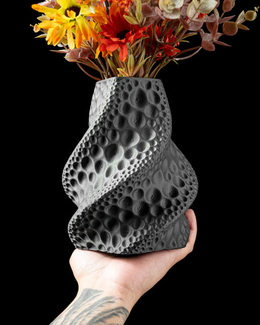 black vase with a gently curved silhouette and deep vertical grooves, flower vase with sculptural moon-like texture, modern vase with concave surfaces resembling lunar craters, vase for dried flowers, decorative stems, or curated floral arrangements, personalized vase with organic symmetry, 3d printed vase for modern home office decor, aesthetic vase in black color with cratered design, vases for flowers or sculptural arrangements, unique home decor centerpiece, elegant and artistic black vase
