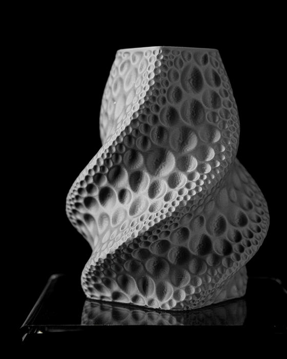 sculptural black vase with lunar crater motif and smooth transitions between convex and concave surfaces, flower vase for dried arrangements or artistic stems, black 3d printed vase with crater pattern spiraling upward in fluid form, personalized vase combining modern design and natural texture, aesthetic vase perfect for contemporary decor, black vase with organic rhythm and balance, home office decor item for dried floral compositions, unique home decor object with cratered facade, modern vase with harmon