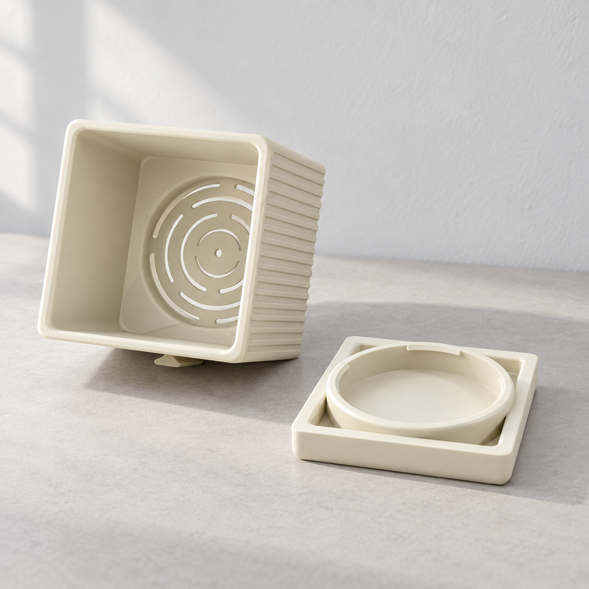 Cream Linor planter tipped sideways to show curved bottom drainage slots beside its separate square base.